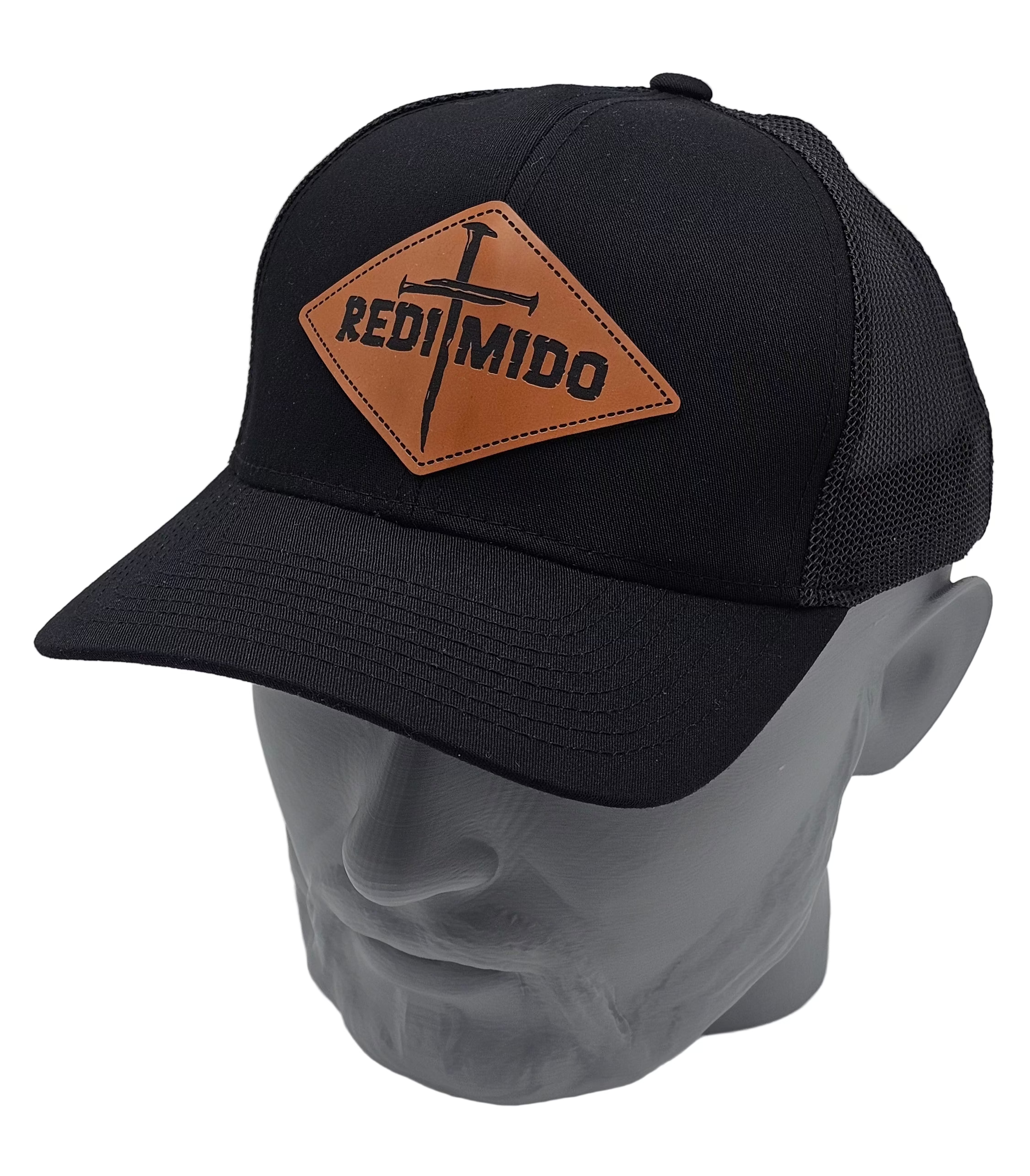 Black cap with a brown leather patch featuring 'Redimido' and two nails forming a cross on a mannequin head against a gray background