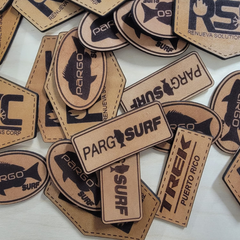 A collection of custom leather patches with various texts embroidered on them, laid out on a surface.